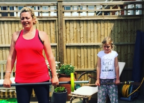 A client in a red vest holding a bar in a garden, a girl standing beside her.