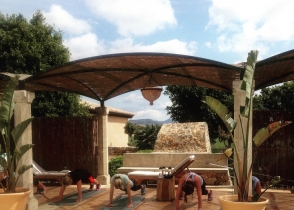 An outdoor session under a shade canopy, people exercising on the ground.