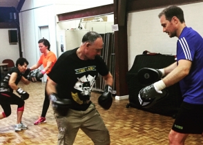 A boxing pads class in a hall, pairs working together.