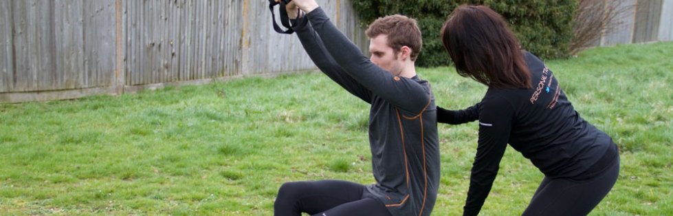 Gemma correcting a client's TRX squat in a garden.