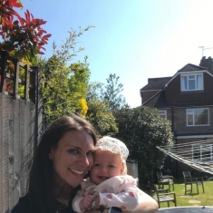 Gemma in her garden holding her baby daughter Willow, both smiling at the camera.
